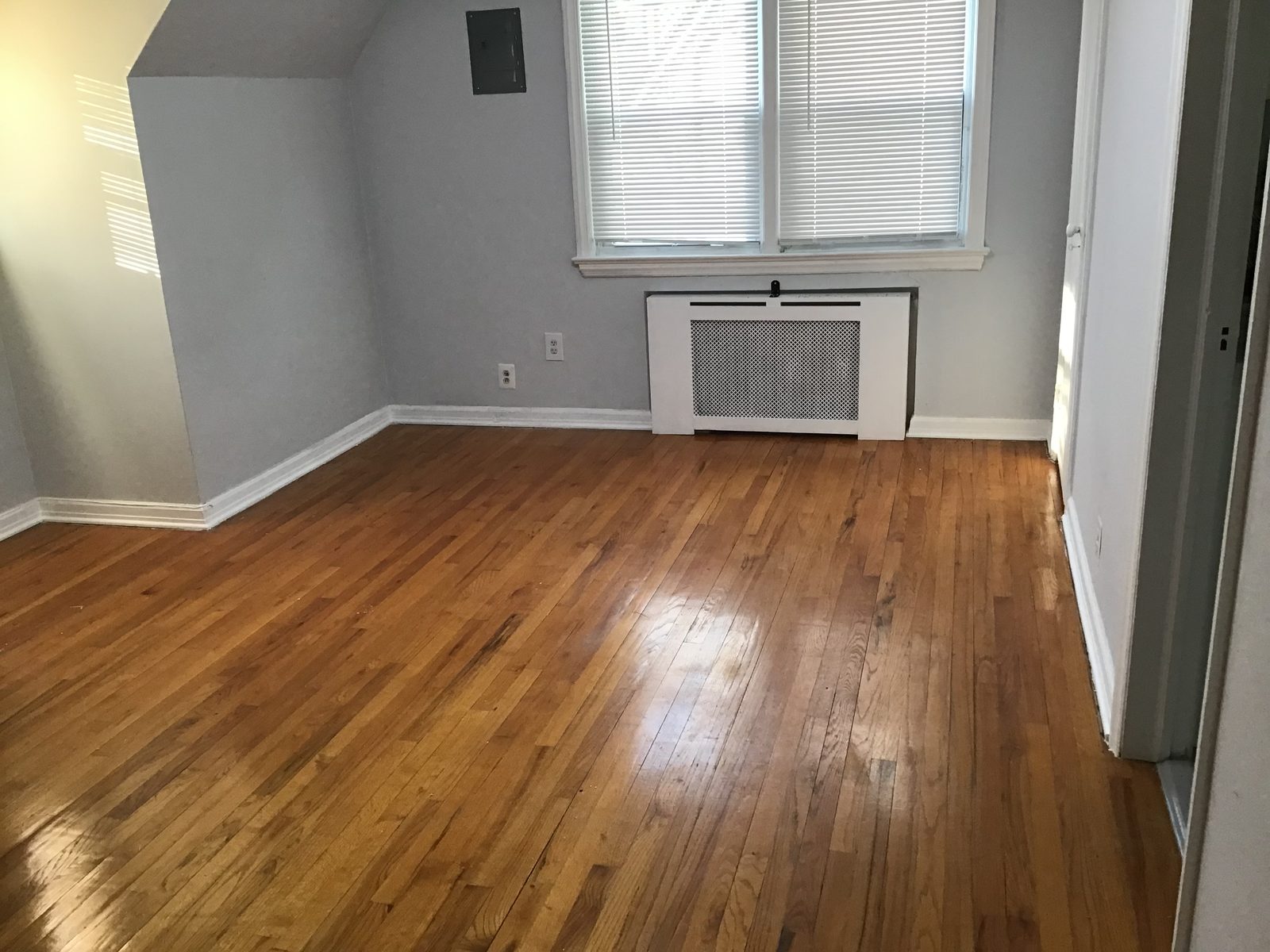 Hardwood floors and a sloped dormer ceiling, with a window over a covered radiator